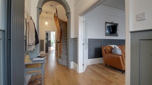 A hallway with a wooden floor, a staircase, a sofa, and a television on the wall. - Belmont Road (Broadstairs)