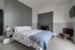 A bedroom with a bed, a nightstand, a chair, a fireplace, and a TV mounted on the wall. - Belmont Road (Broadstairs)