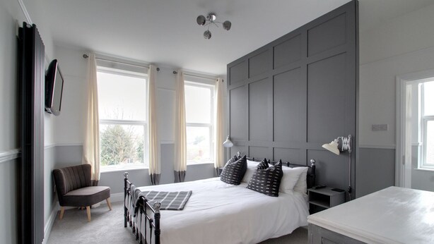 A bedroom with a large bed, bedside tables, a chair, and a radiator. - Belmont Road (Broadstairs)