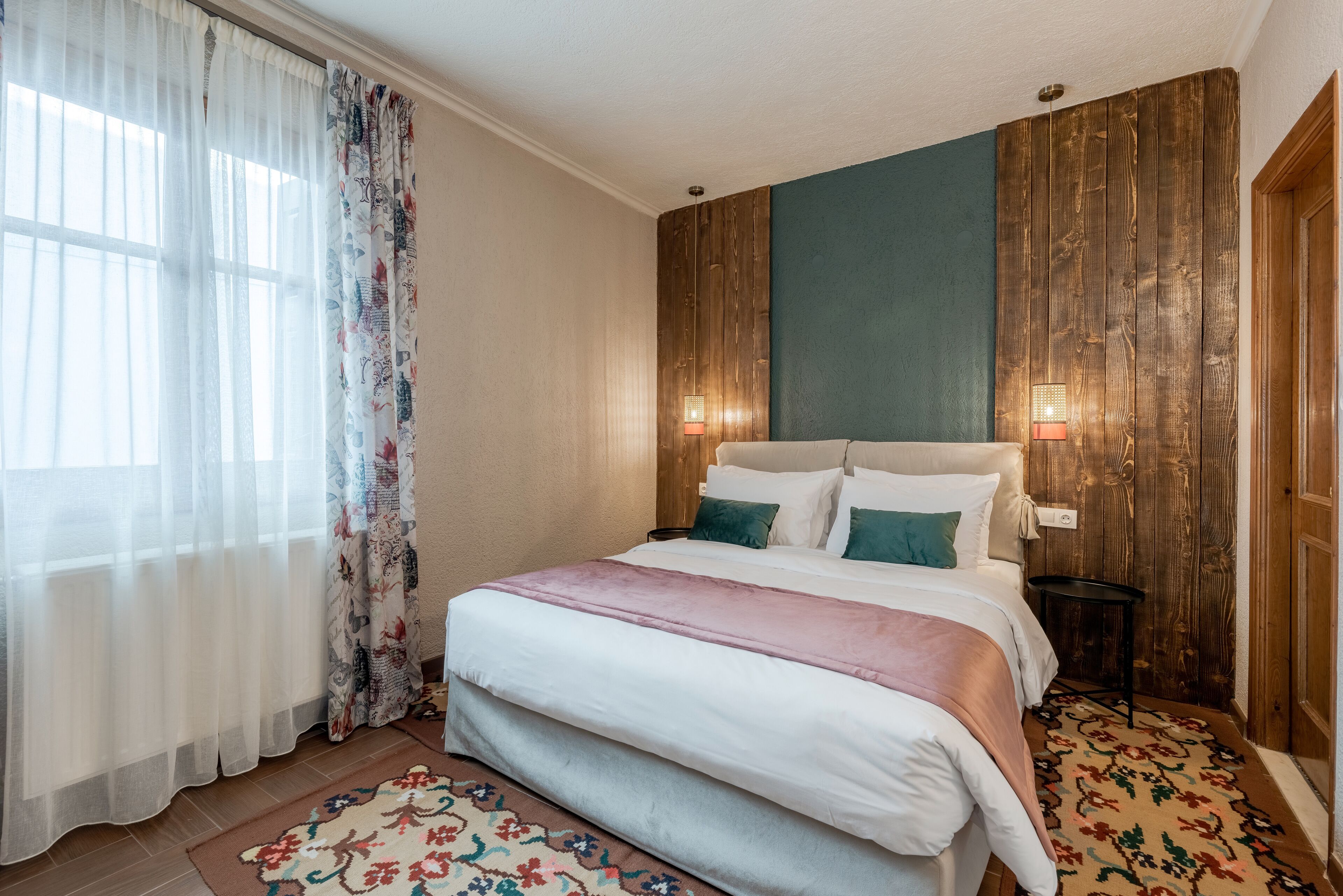 A bedroom with a bed, curtains, a nightstand, and a wall-mounted lamp.