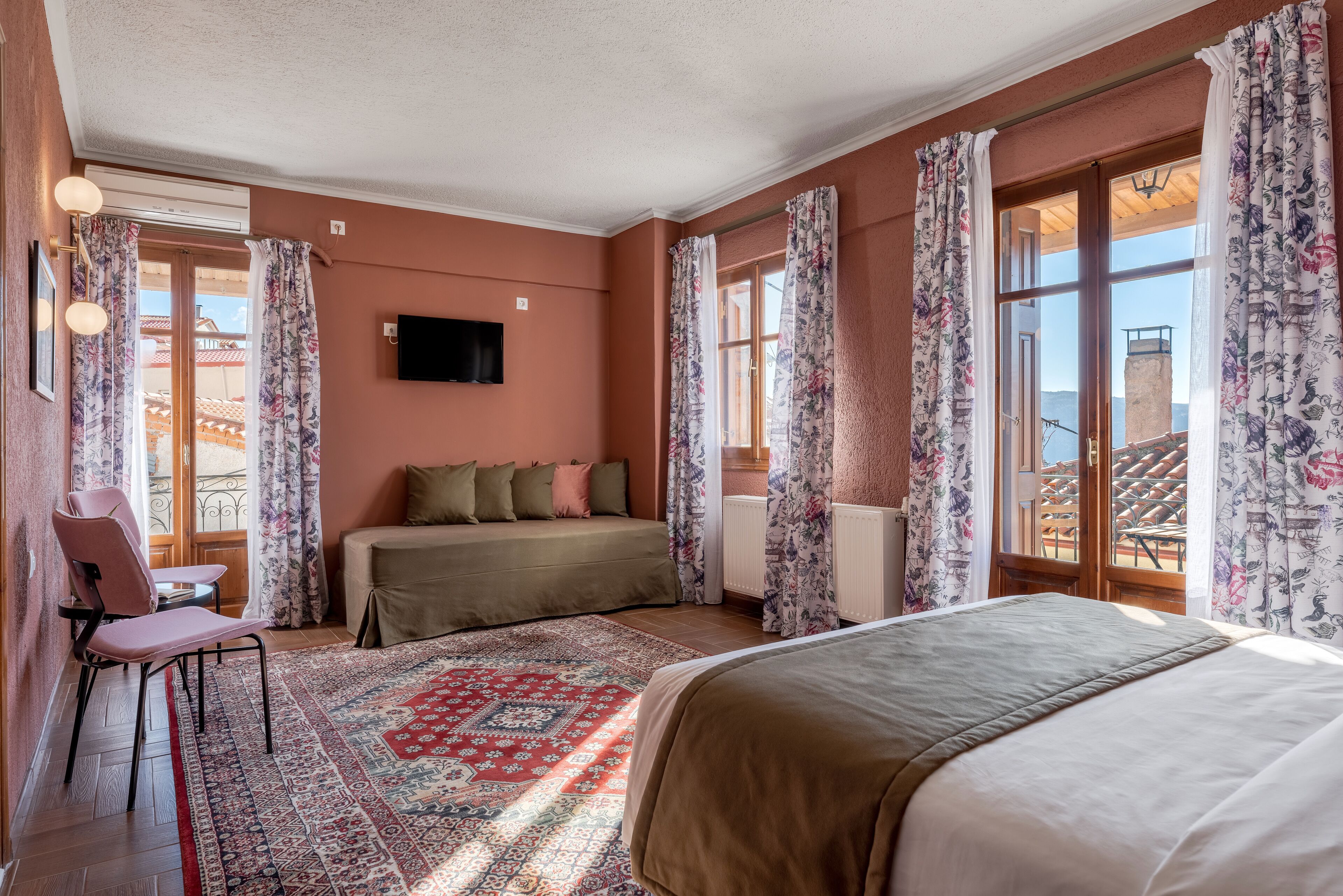 A bedroom with a bed, a sofa, a chair, a TV, and a view of the outside.
