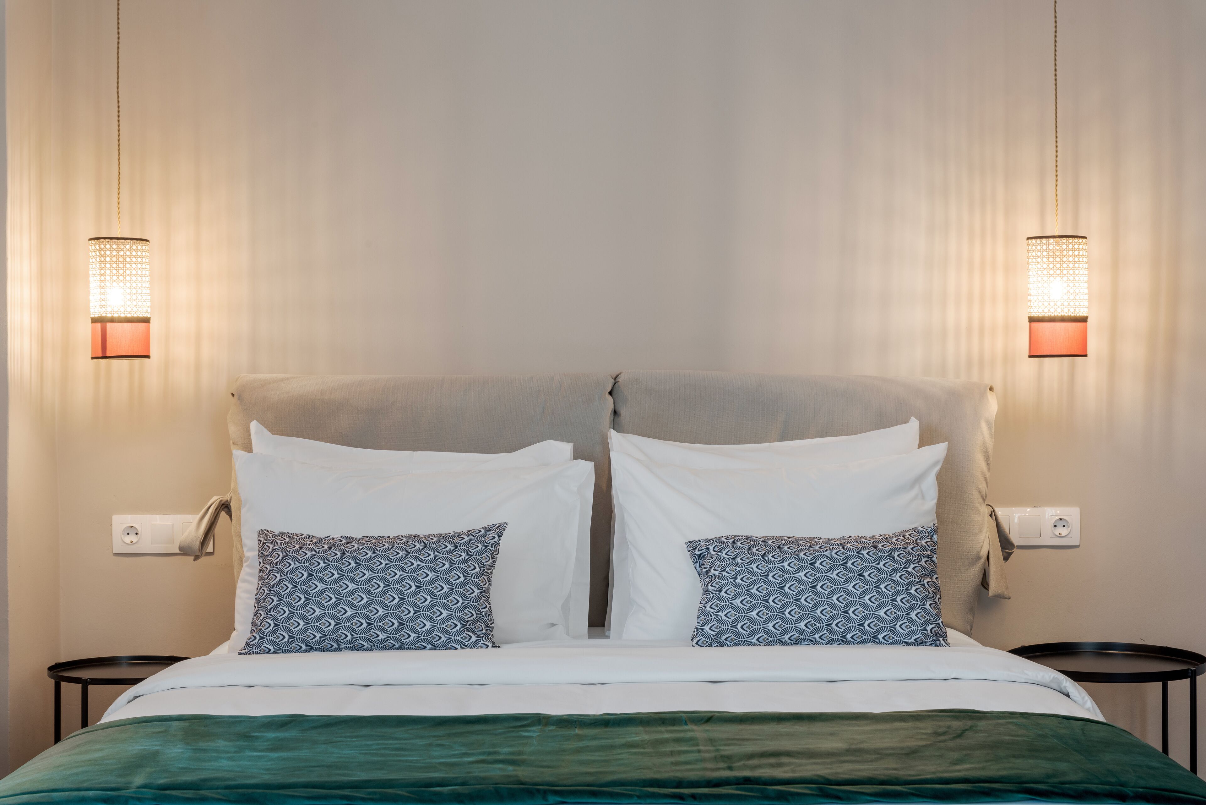 Una cama bien hecha con almohadas blancas y estampadas, un edredón verde y dos mesitas de noche con lámparas.