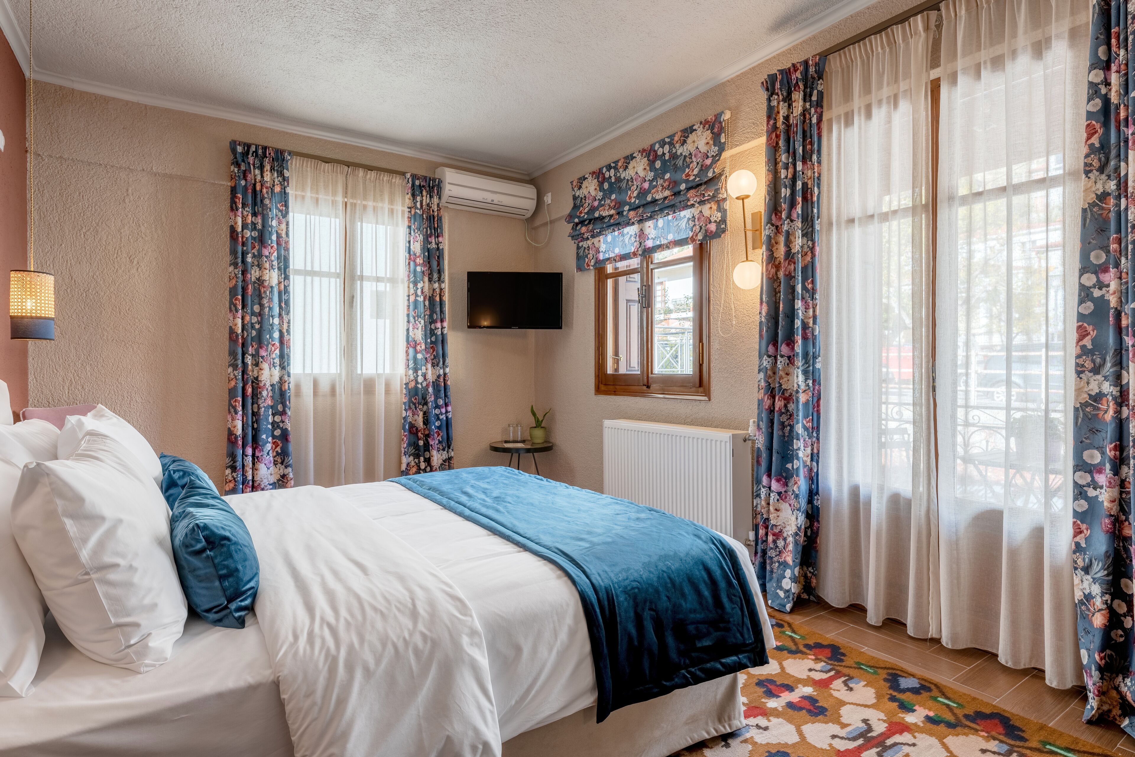 A bedroom with a bed, floral curtains, a TV, and a window with a view.