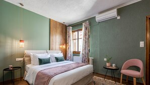 Quarto com cama, uma mesinha com planta, uma cadeira e um ar condicionado.