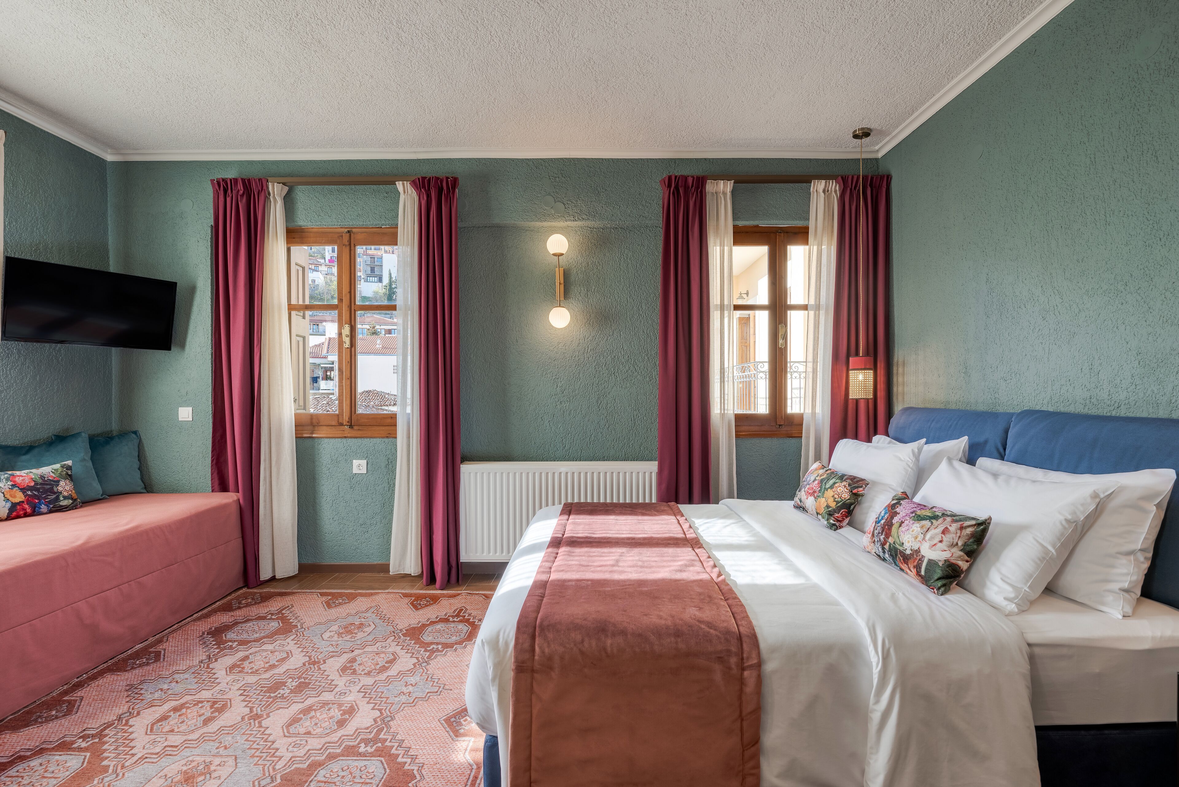 Una habitación con cama, sofá, televisión y ventana con cortinas.
