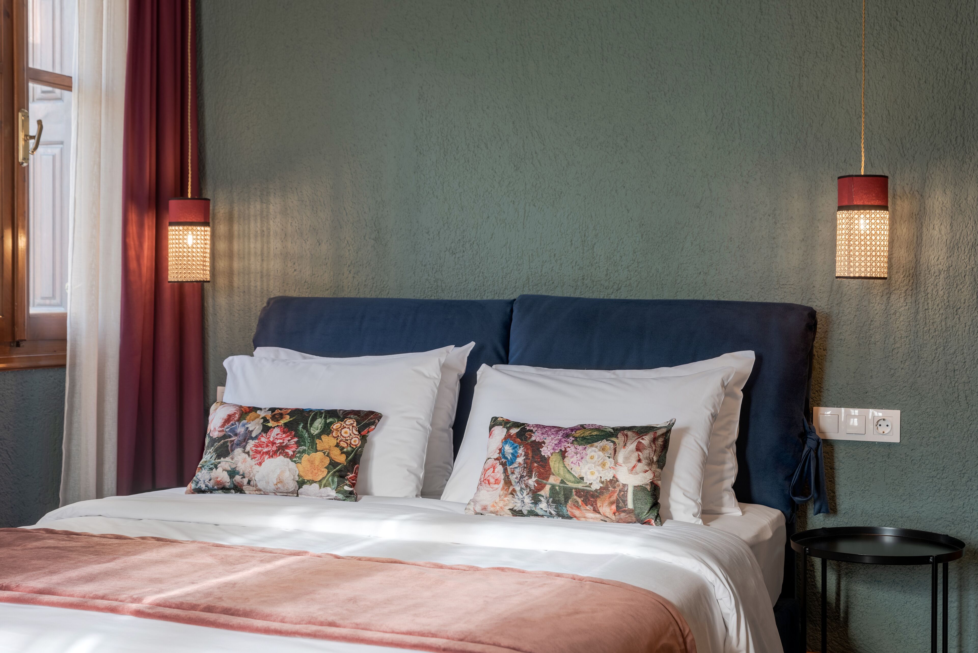 Ein ordentlich bezogenes Bett mit floralen Kissen, einem blauen Kopfteil und zwei Wandlampen.