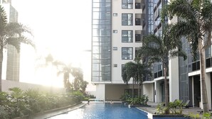 Une piscine dont le bord est recouvert de carreaux, entourée de palmiers et de bâtiments modernes.