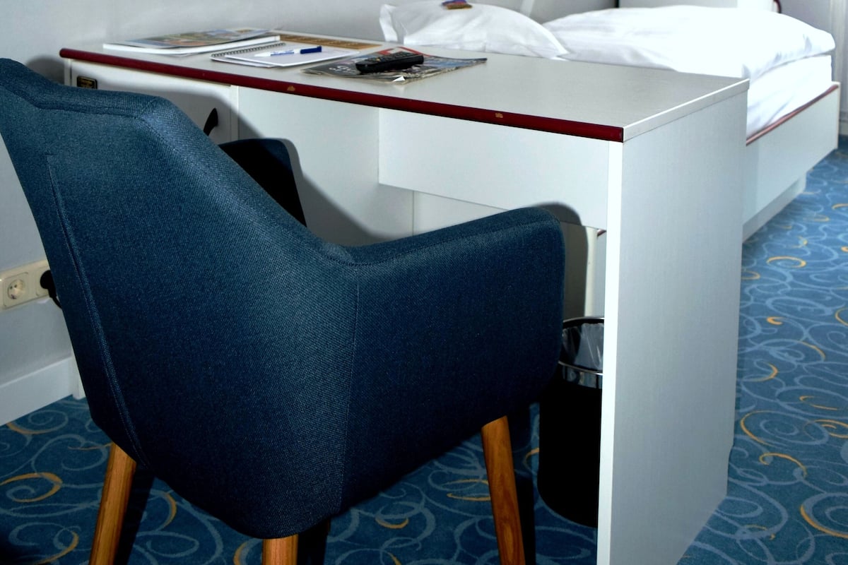A hotel room with a desk, chair, bed, TV, and a unique ceiling design.