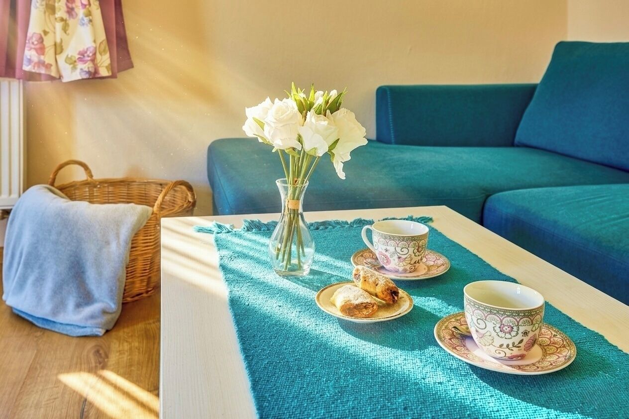 A room with a teal sofa, a wicker basket, a vase with white flowers, and a table with a teapot and teacups.