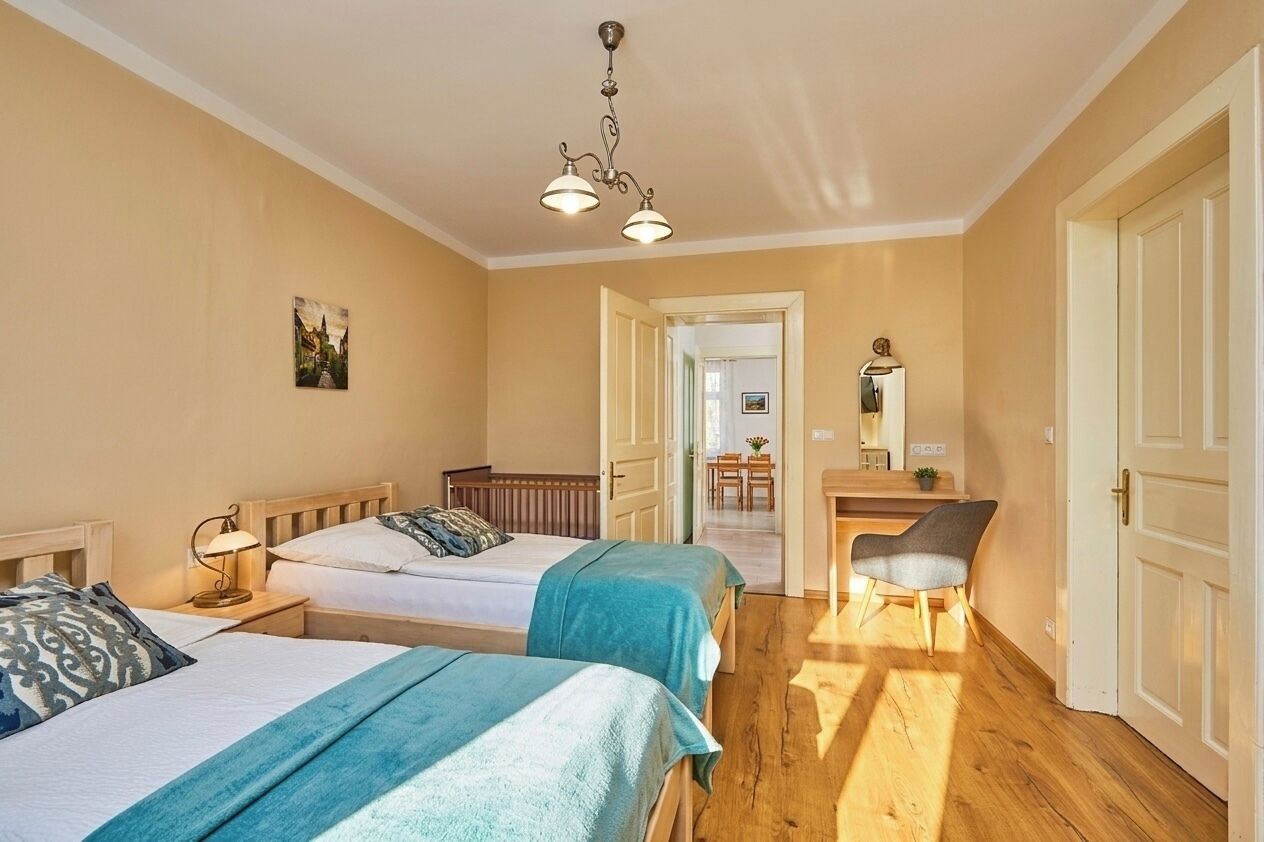 Een hotelkamer met twee bedden, een bureau, een stoel en een gang naar een andere kamer.