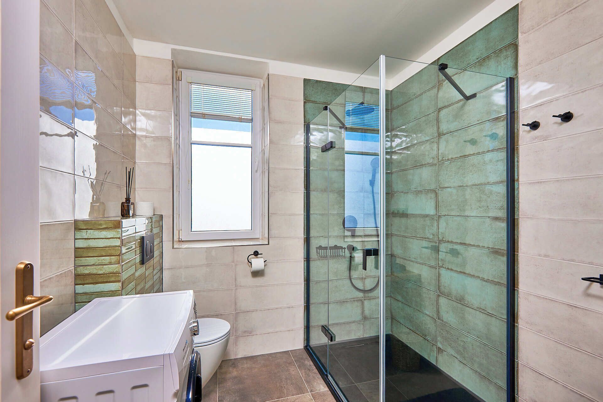 Un baño moderno con cabina de ducha de vidrio, un lavabo blanco y una ventana.