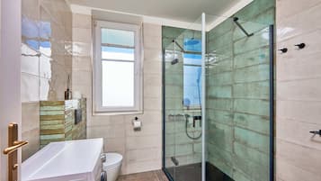 Un baño moderno con cabina de ducha de vidrio, un lavabo blanco y una ventana.