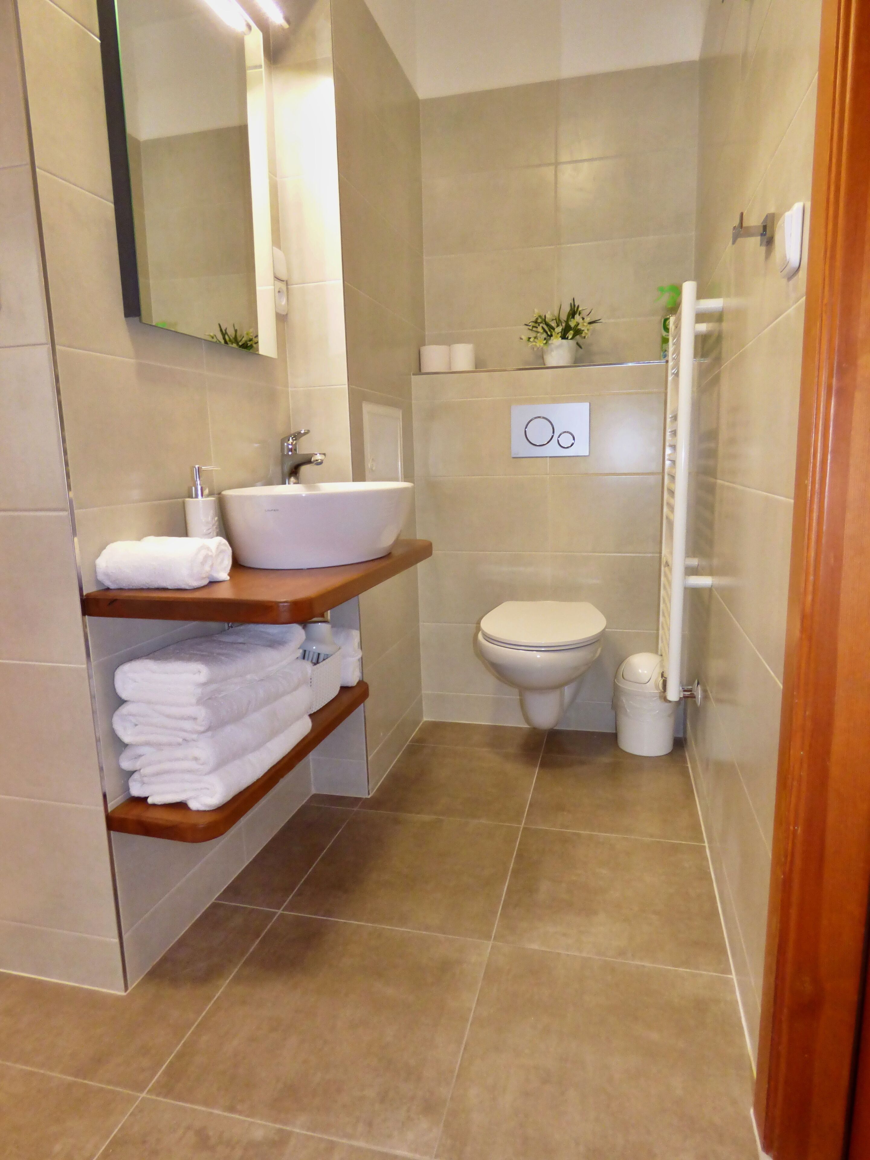 Een badkamer met een wastafel, toilet en douche. Handdoeken en toiletartikelen liggen op planken.
