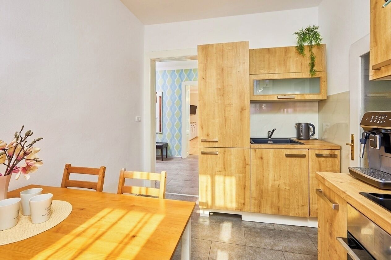 A modern kitchen with wooden cabinets, a coffee machine, and a dining area with a table and chairs.