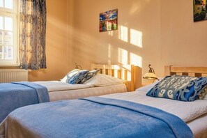 Una habitación con dos camas, una ventana con cortinas, una lámpara y un cuadro en la pared.