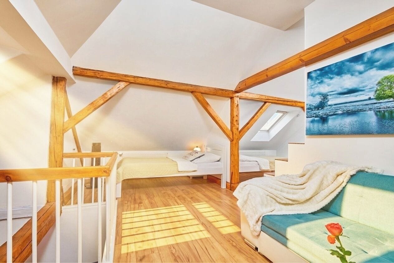 Un dormitorio tipo loft con techo inclinado, vigas de madera, una cama, un sofá y un cuadro.