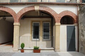 A building with a beige facade, two windows with metal bars, a grey door, and a small balcony with potted plants. - la vigna in Città il vigneto (Verona)