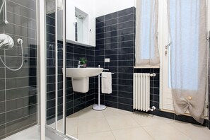 A modern bathroom with a glass shower enclosure, a white sink, and a black tiled wall. - la vigna in Città il vigneto (Verona)