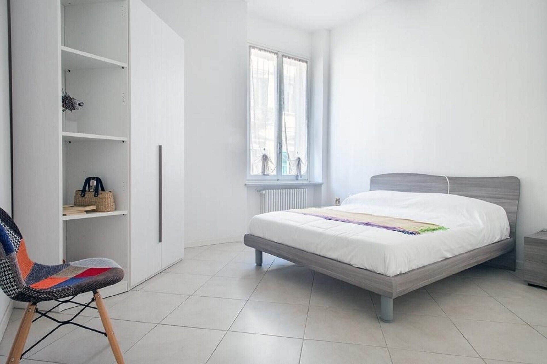 Un dormitorio con cama, una silla, un armario y una ventana.