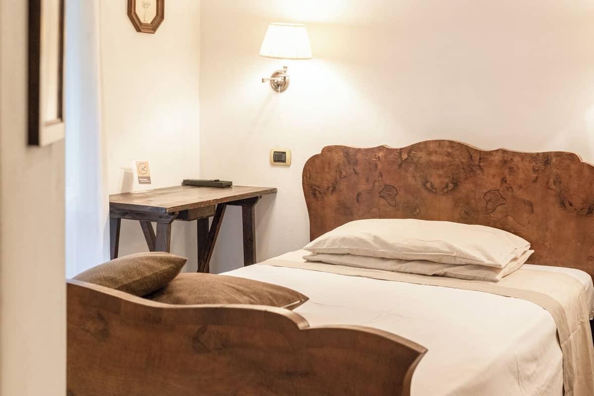 A hotel room with a wooden headboard, a bed with white linens, a small table, and a wall-mounted lamp.