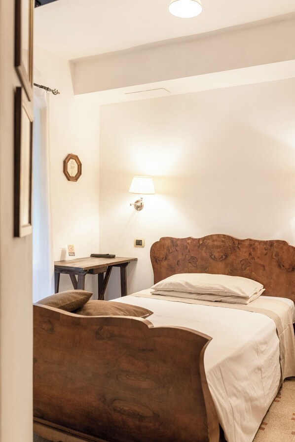 A hotel room with a wooden headboard, a bed with white linens, a small table, and a wall-mounted lamp.