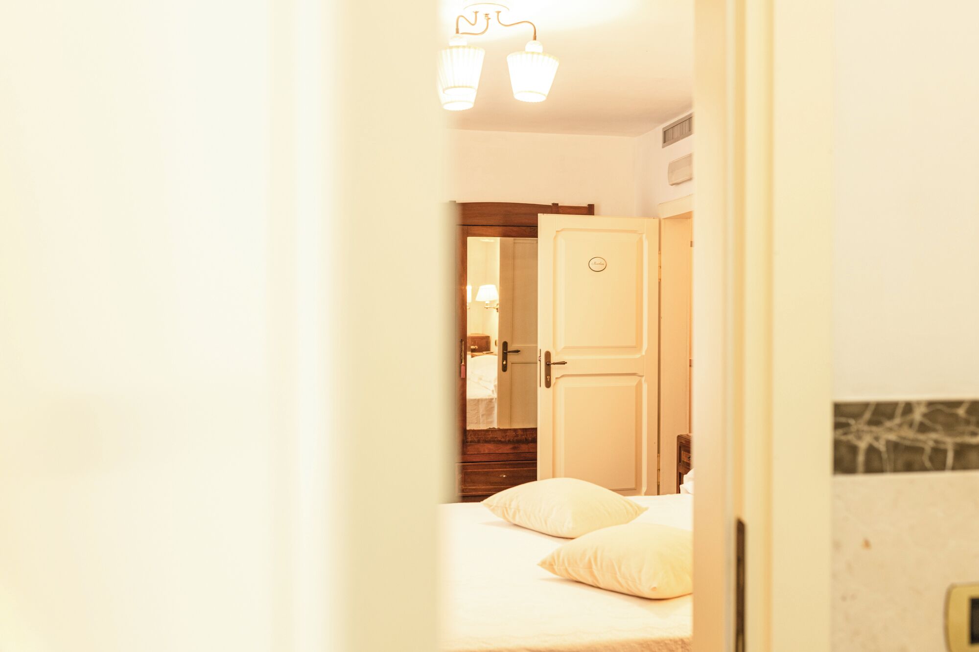 Ein Hotelzimmer mit Bett, Kissen, einem Nachttisch, einem Spiegel und einer Tür mit einem Schild.