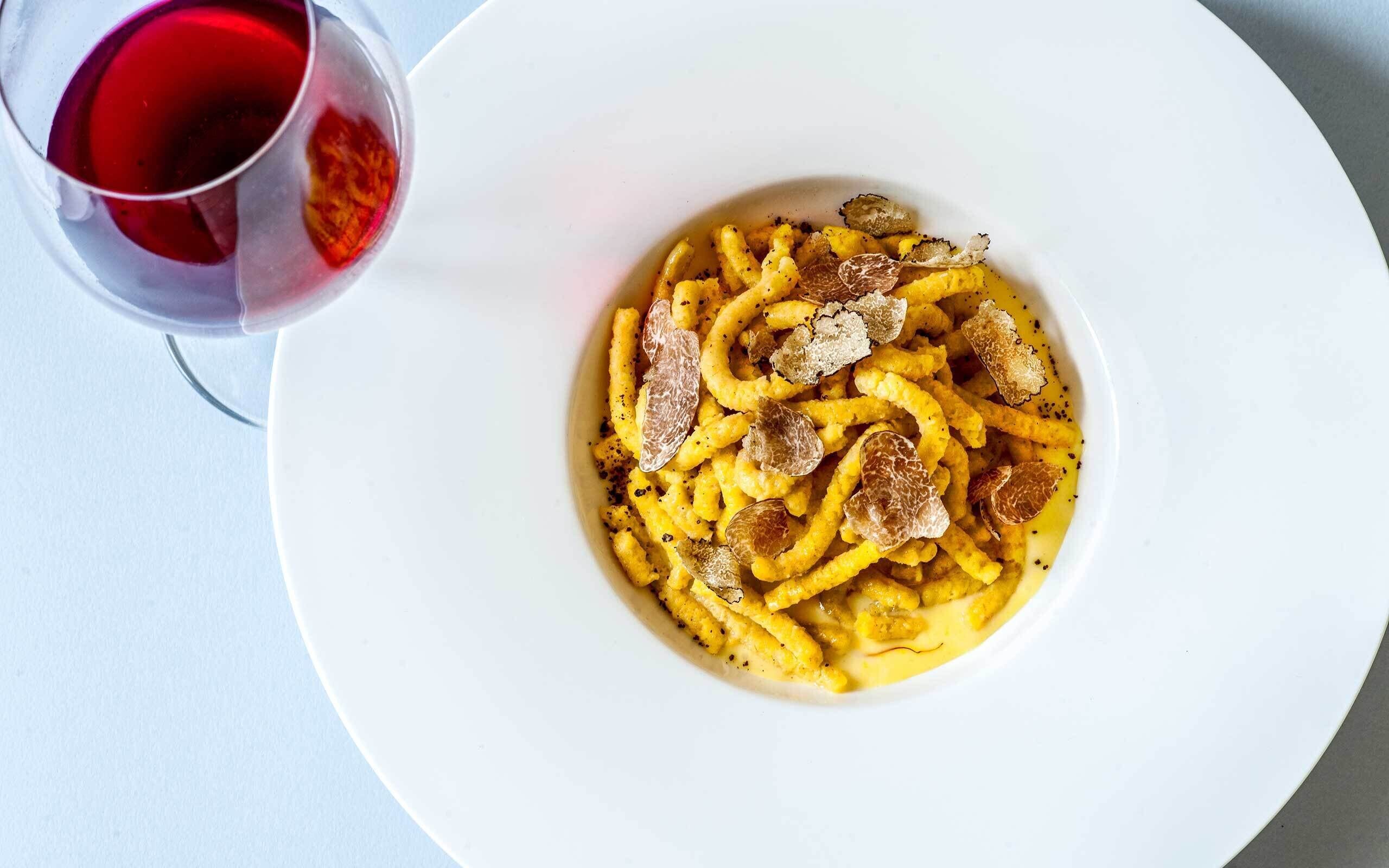 A plate of pasta with truffles and a glass of red wine.