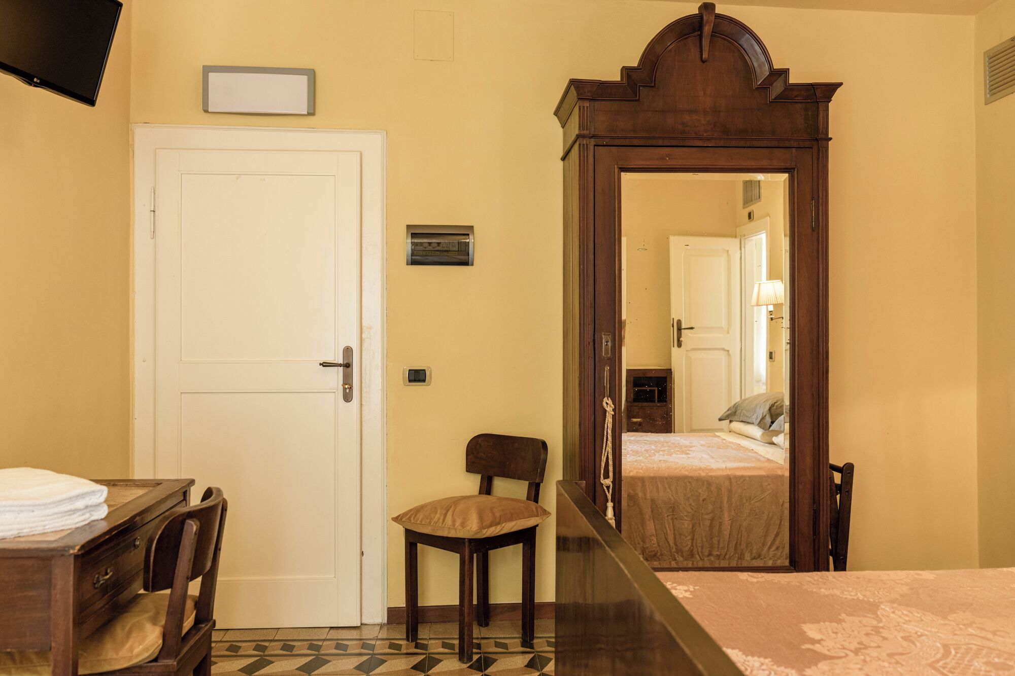 Une chambre d’hôtel comprenant un lit, un bureau avec une chaise, une armoire, un miroir et une porte.