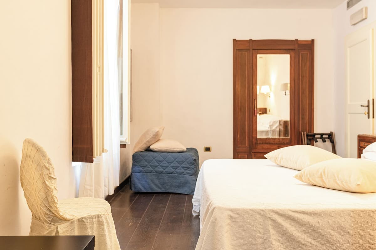 A bedroom with a bed, a chair, a wooden door, and a mirror.