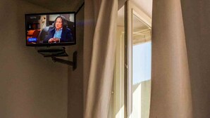 Ett rum med en tv som är monterad på väggen, ett fönster med gardiner och en bänk.