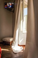 Una habitación con televisión montada en la pared, una ventana con cortinas y un banco.