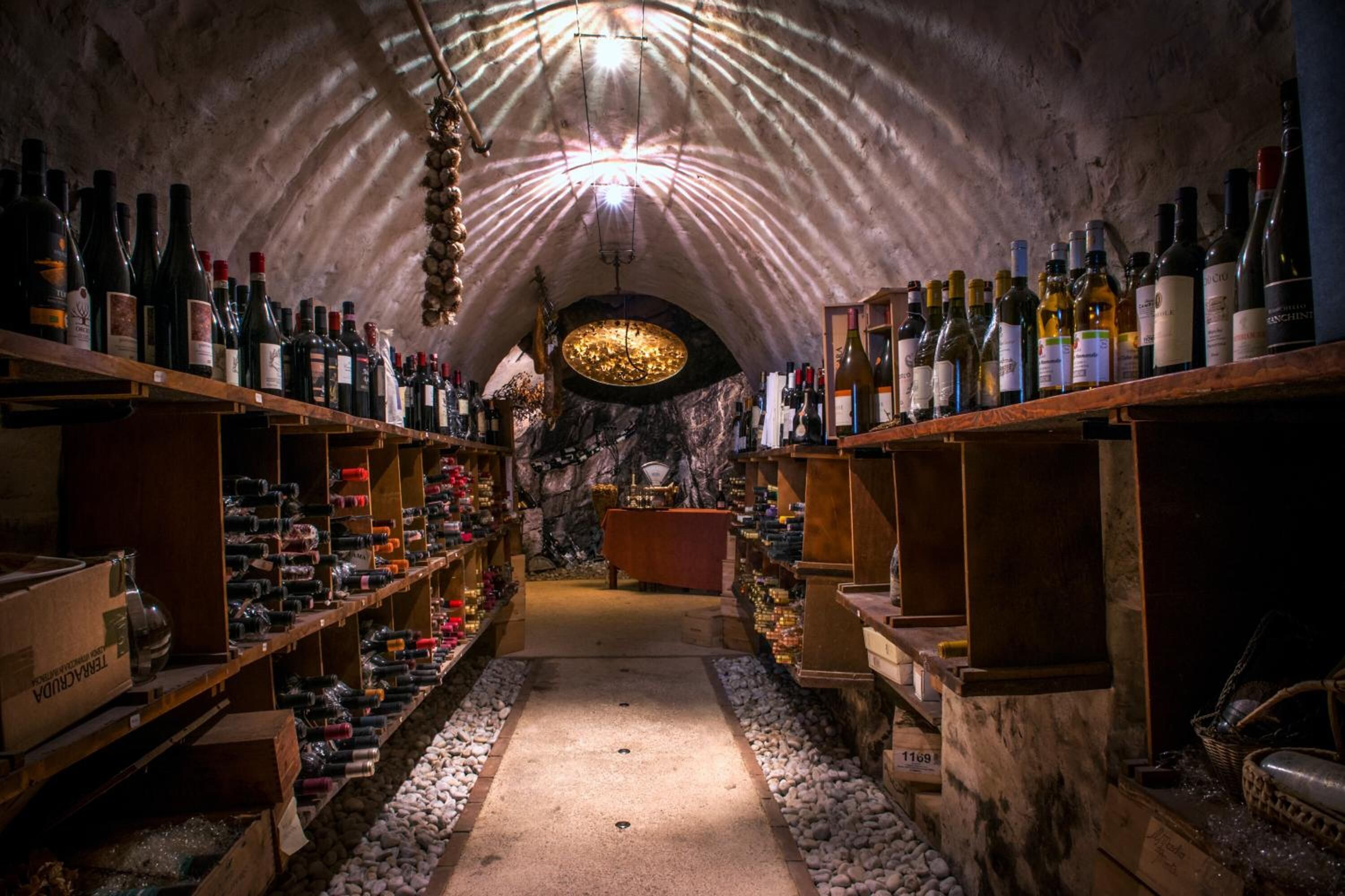 Una bodega subterránea con estantes llenos de botellas de vino y una mesa central.