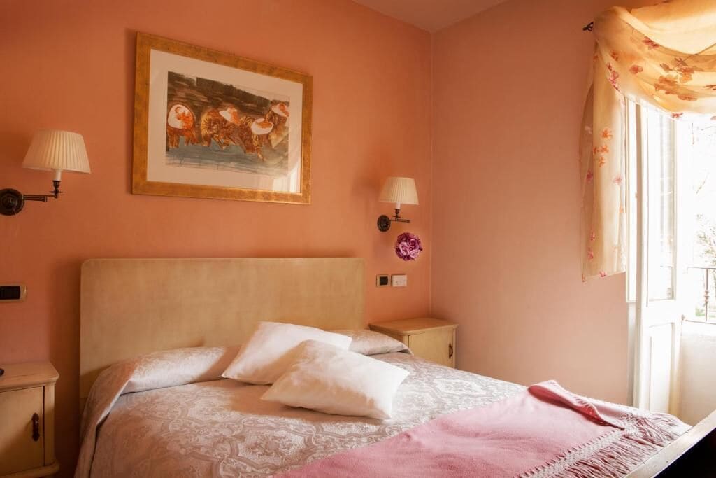 Une chambre à coucher avec un lit, deux lampes fixées au mur, un tableau encadré et une fenêtre avec des rideaux.