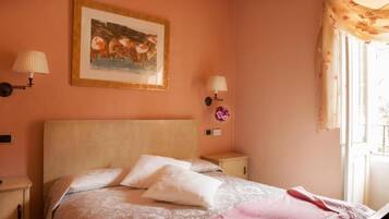 Une chambre à coucher avec un lit, deux lampes fixées au mur, un tableau encadré et une fenêtre avec des rideaux.