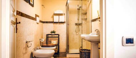 Un baño con inodoro, bidé y lavamanos, ducha y toallero de pared.