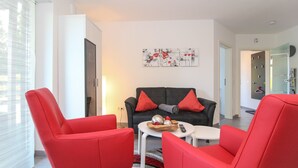 Ein modernes Wohnzimmer mit roten Sesseln, einem schwarzen Sofa und einem kleinen Tisch mit einer Schüssel und einer Fernbedienung.
