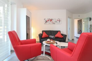 Un salon moderne avec des fauteuils rouges, un canapé noir et une petite table sur laquelle se trouvent un bol et une télécommande.