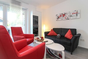 Un salon moderne avec un canapé noir, des fauteuils rouges, une table basse et une bibliothèque.
