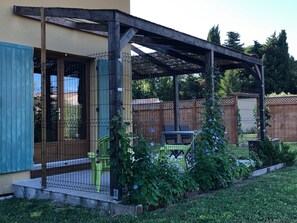 Un patio cubierto con una pérgola de madera, un jardín vallado y una zona de estar con sillas.