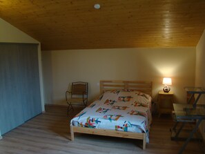 Une chambre avec un plafond en bois, un lit recouvert d’une couvre-lit aux motifs colorés, une chaise, une table de chevet avec une lampe et un bureau avec une chaise.