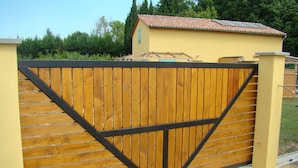 A wooden gate with a black metal frame, leading to a yellow building with a tiled roof. - House with terrace, Avignon festival 12km away, Spirou park and wave island (Le Thor)