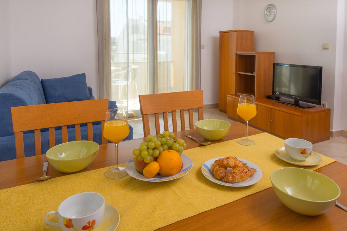 A dining area with a table set for breakfast, including fruits, croissants, and beverages.