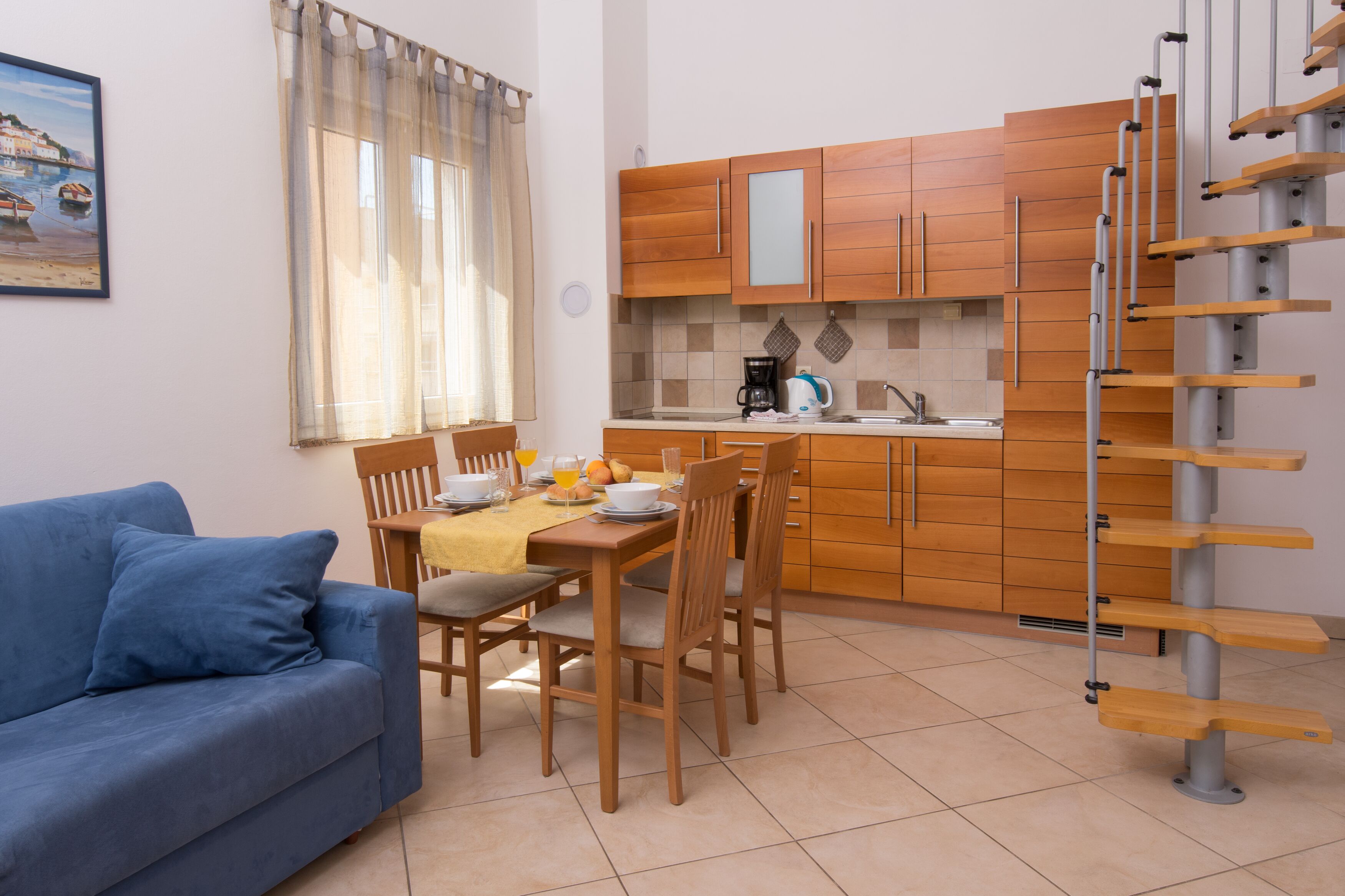 Eine moderne Küche mit Holzschränken, einem Esstisch mit Stühlen und einem blauen Sofa im Wohnbereich.