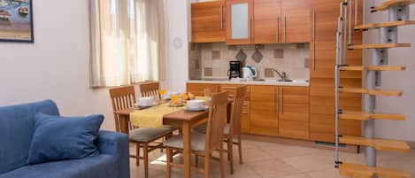 A modern kitchen with wooden cabinets, a dining table with chairs, and a blue sofa in a living area.