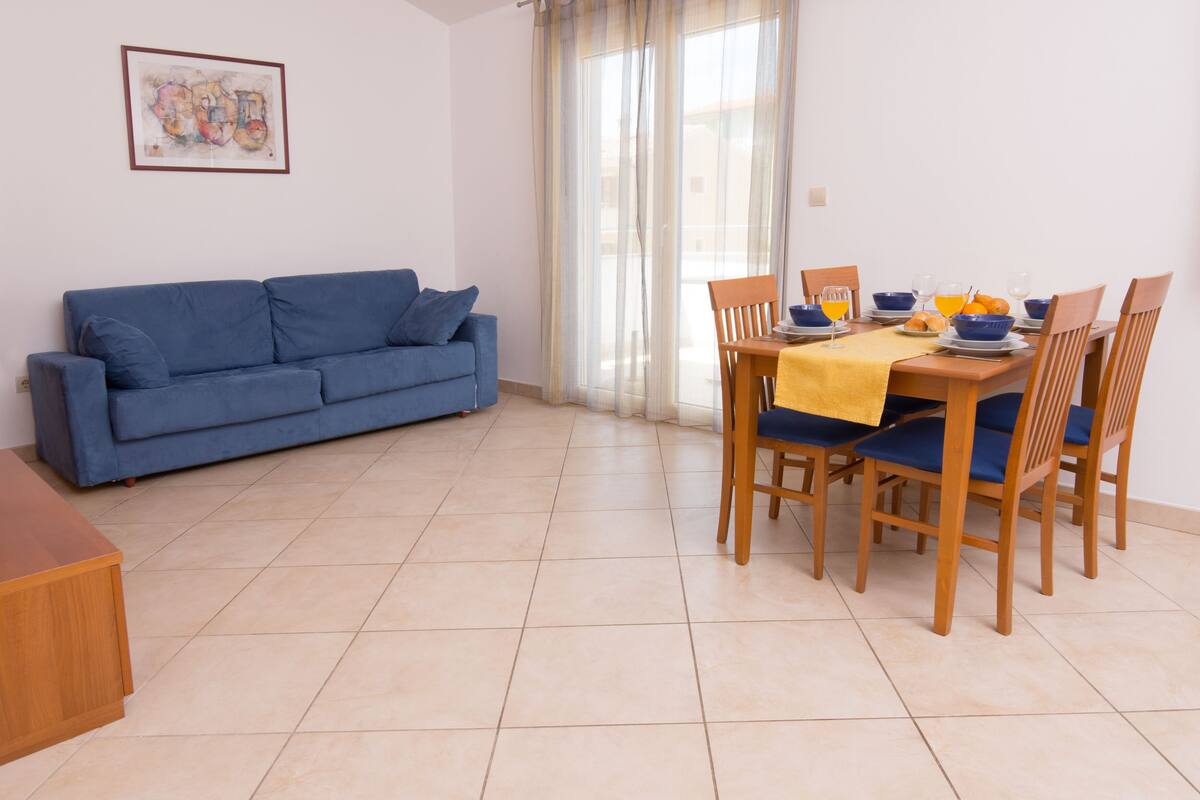 A dining area with a table set for four, blue chairs, and a blue sofa in the background.