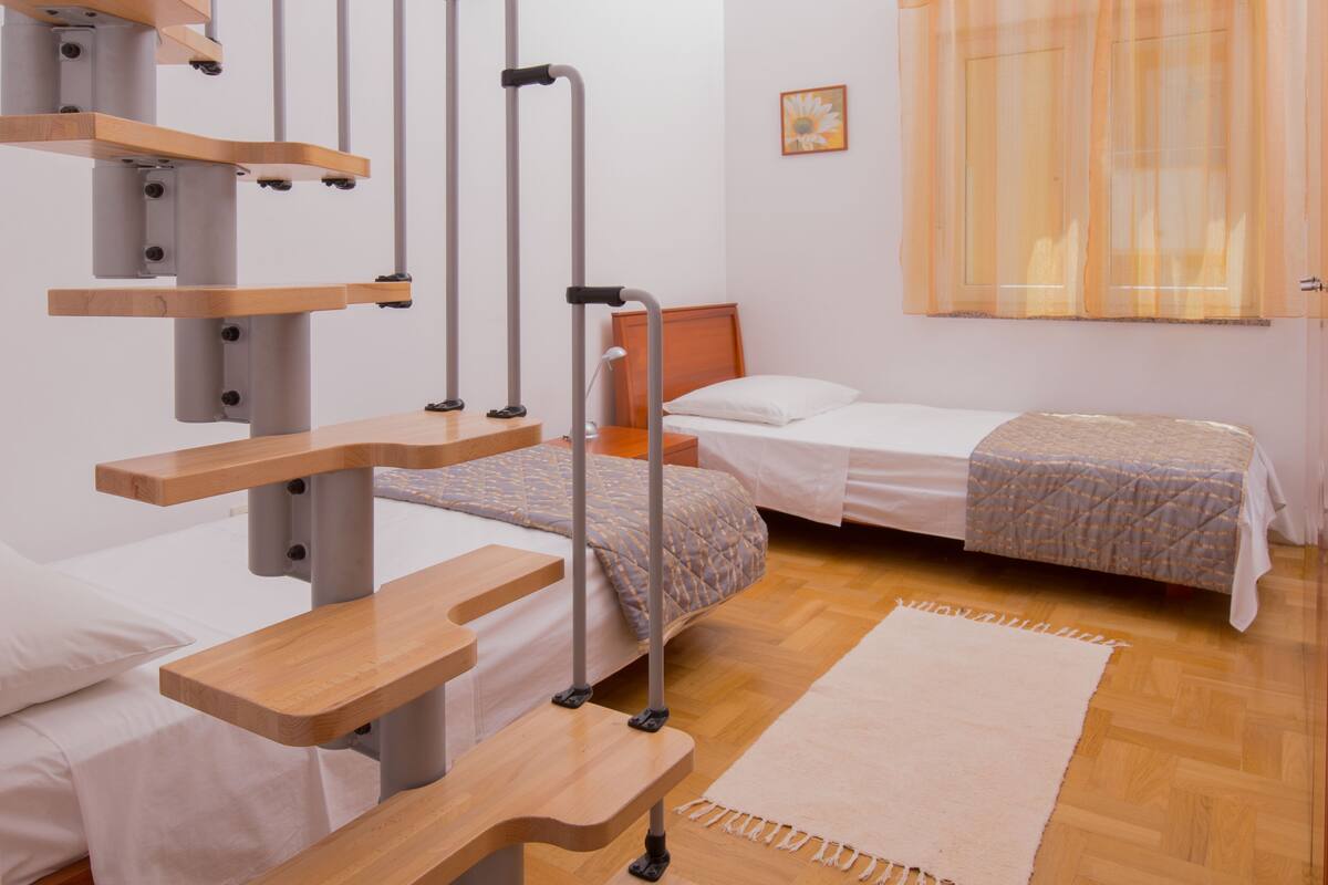 A room with two beds, a wooden desk, and a window with curtains.