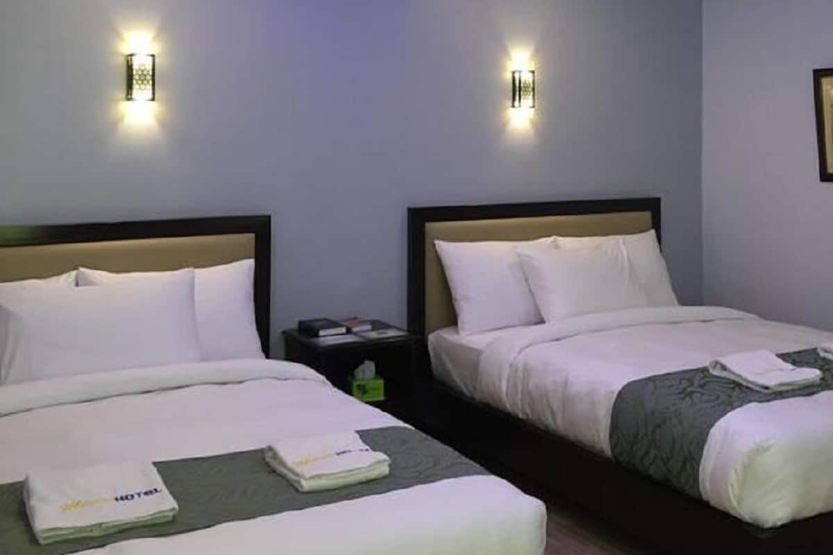 Habitación de hotel con dos camas, cada una con cabecera, mesita de noche y lámpara de pared.
