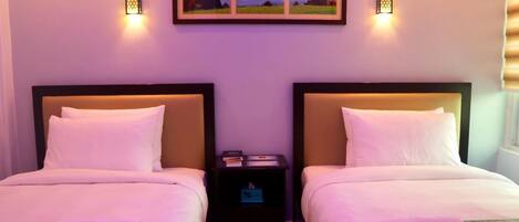 Habitación de hotel con dos camas, cada una con cabecera y almohada con el nombre del hotel. Hay luces fijadas a la pared y un cuadro enmarcado sobre las camas.
