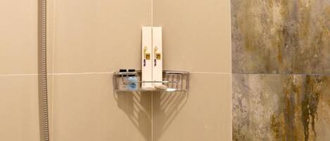 A shower with a handheld showerhead and a wall-mounted faucet. There is a shelf with toiletries and a towel rack.