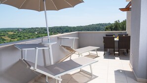 Un balcón con mesa y sillas, una sombrilla colgante y vistas a un paisaje verde.